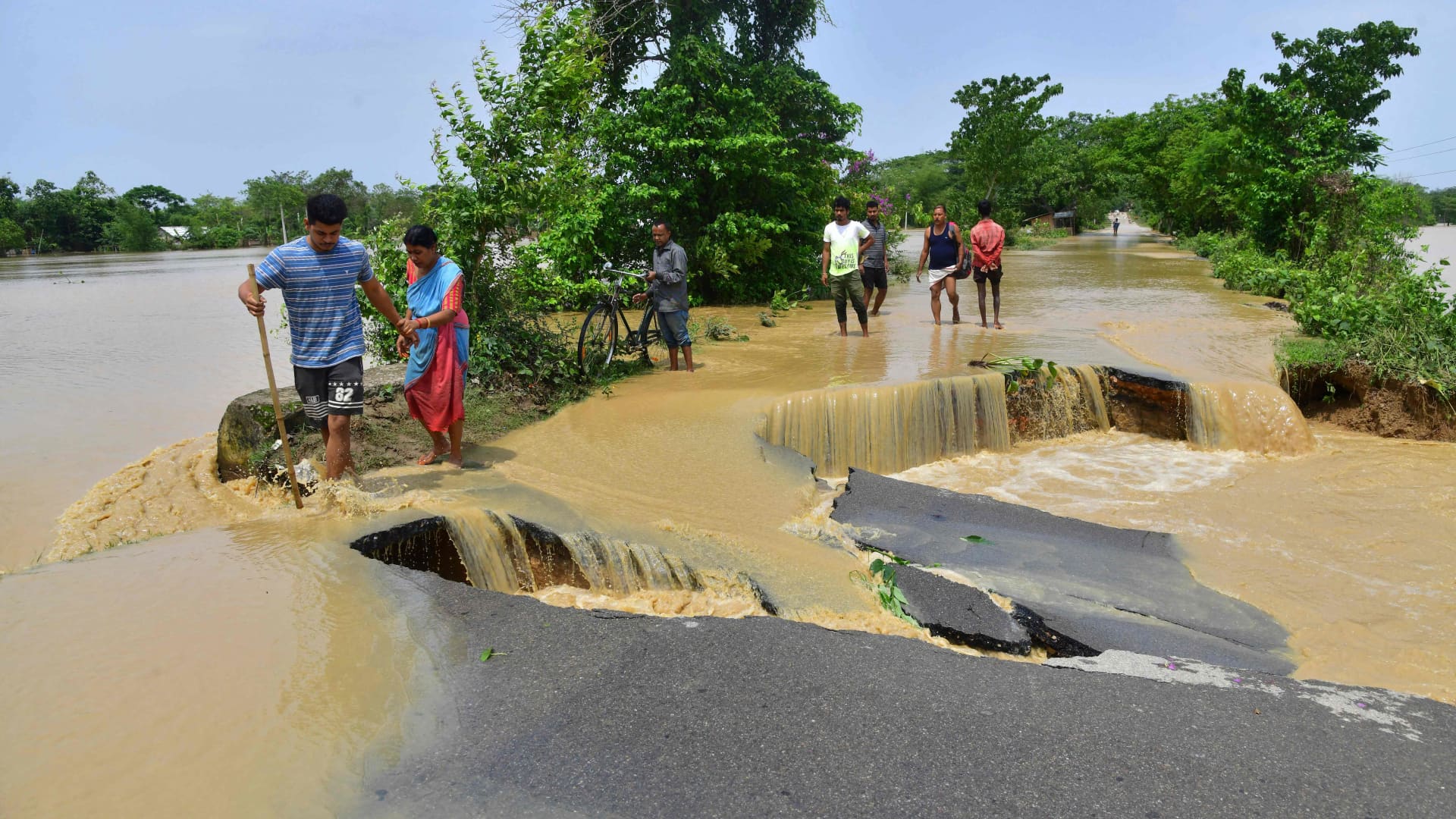 People wade through a road damaged by flood waters after heavy rains in Nagaon district, Assam state, on May 19, 2022.