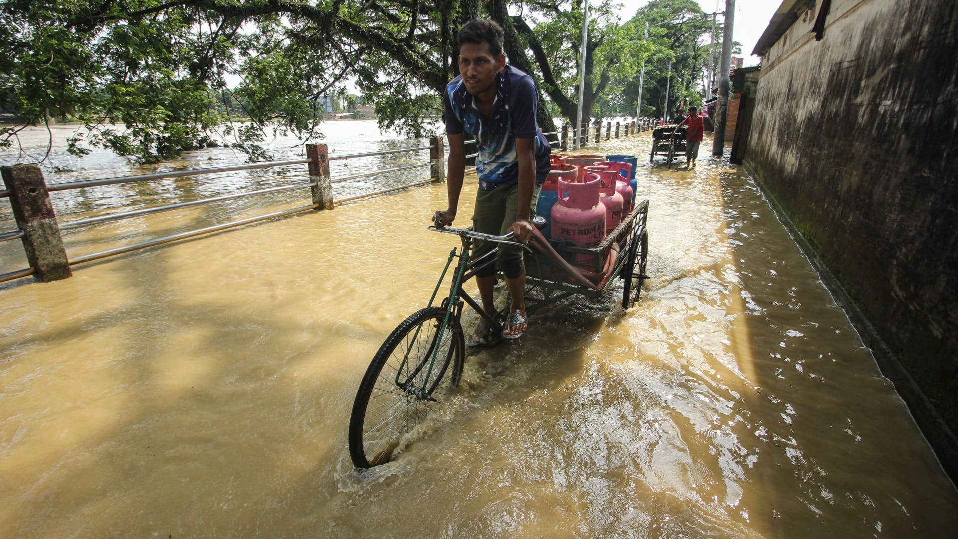 A man transports Liquefied Petroleum Gas (LPG) cylinders on a on a rickshaw van along a path next to the banks of the overflown Surma River following heavy rainfalls in Sylhet, Bangladesh on May 19, 2022.