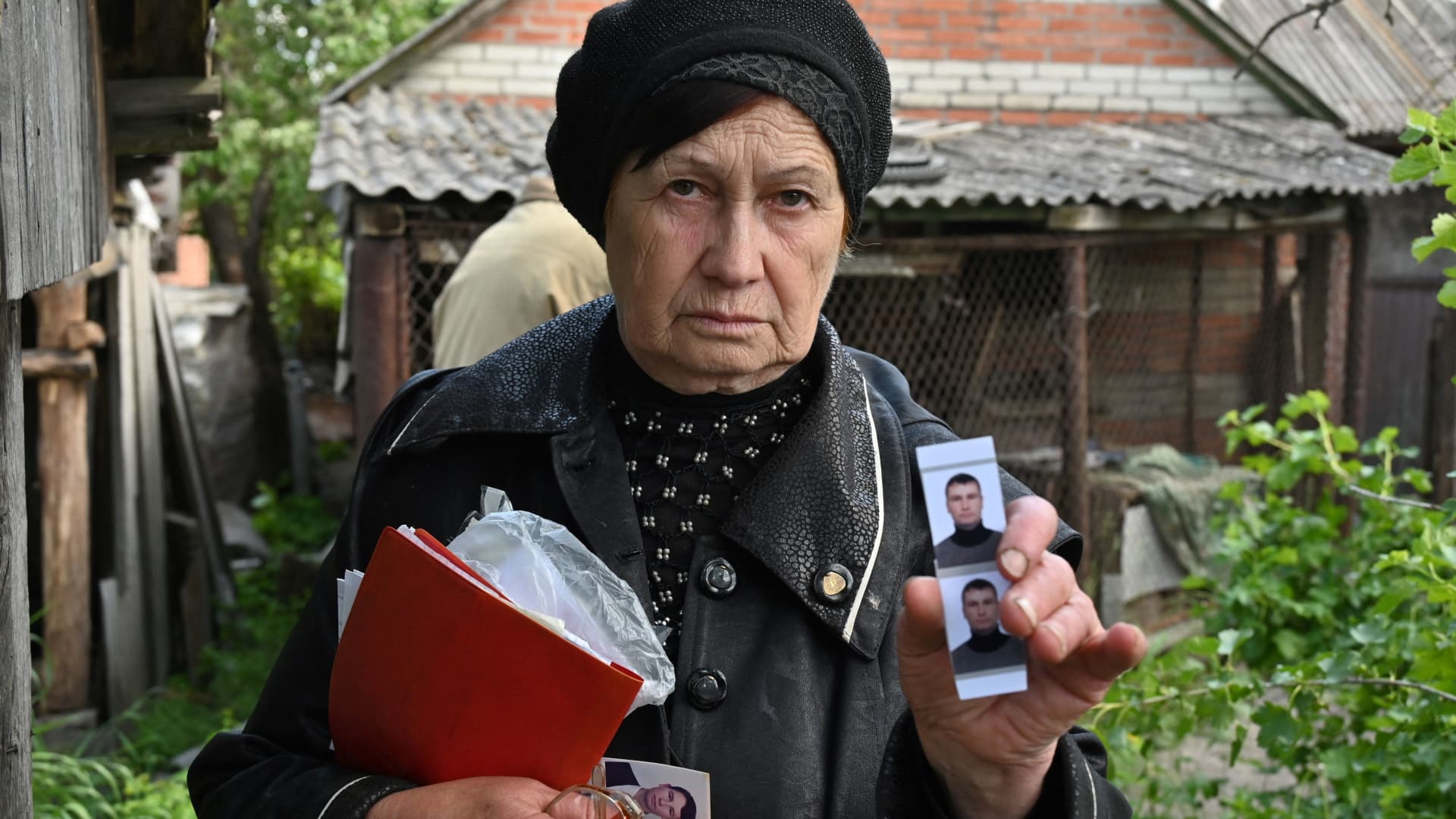 Olga Khomenko, 67, shows pictures of her son, a 38-year-old local man who allegedly died when his car was hit by a shell of Russian tank and was buried in the courtyard of his house while Ukrainian police forensics exhum his remains in the village of Mala Rogan, near Kharkiv on May 23, 2022.