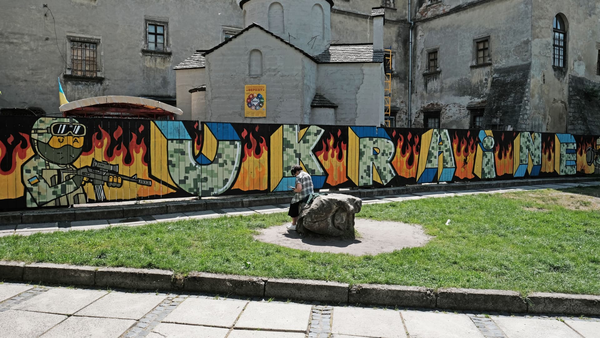 A woman sits in front of a graffiti tribute to the Ukrainian Military and their ongoing war with Russia.