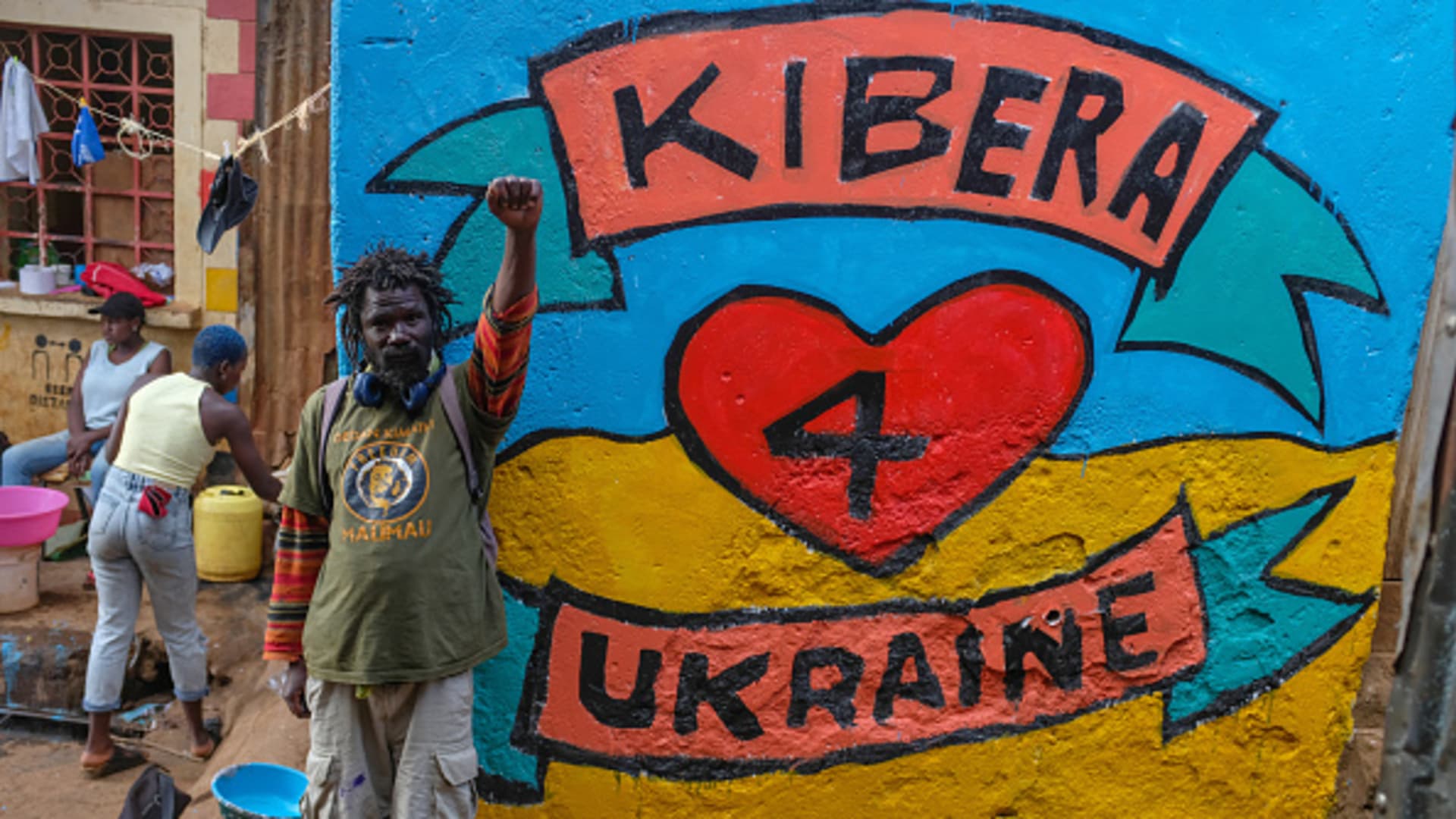 An artist showing a protest symbol power sign by a street mural created by a group of Artists from Maasai Mbili depicting Kibera's love for Ukraine a midst the war.