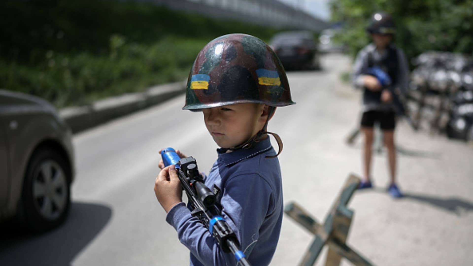 STOYANKA, UKRAINE - MAY 27: Ukrainian boys Andrii, aged 12 and his friend Valentyn 6, play at being soldiers and man their makeshift checkpoint in their village next to a school crossing. The two boys have become well known to passing motorists on May 27, 2022 in Stoyanka, Ukraine. As Russia concentrates its attack on the east and south of the country, residents of the Kyiv region are returning to assess the war's toll on their communities. The towns around the capital were heavily damaged following weeks of brutal war as Russia made its failed bid to take Kyiv.(Photo by Christopher Furlong/Getty Images)