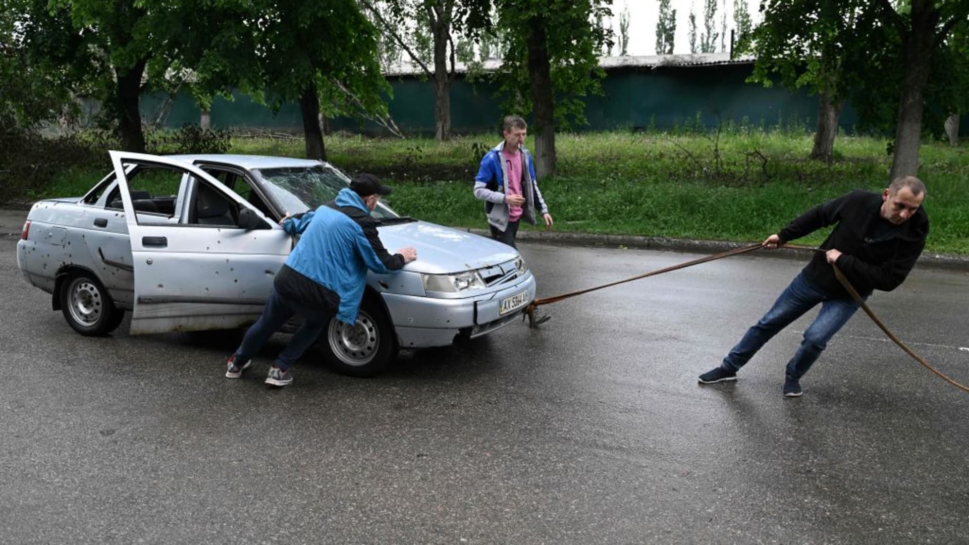 Local residents try to tow a damaged car in the Saltivka district, northern Kharkiv on May 29, 2022, amid Russian invasion of Ukraine.