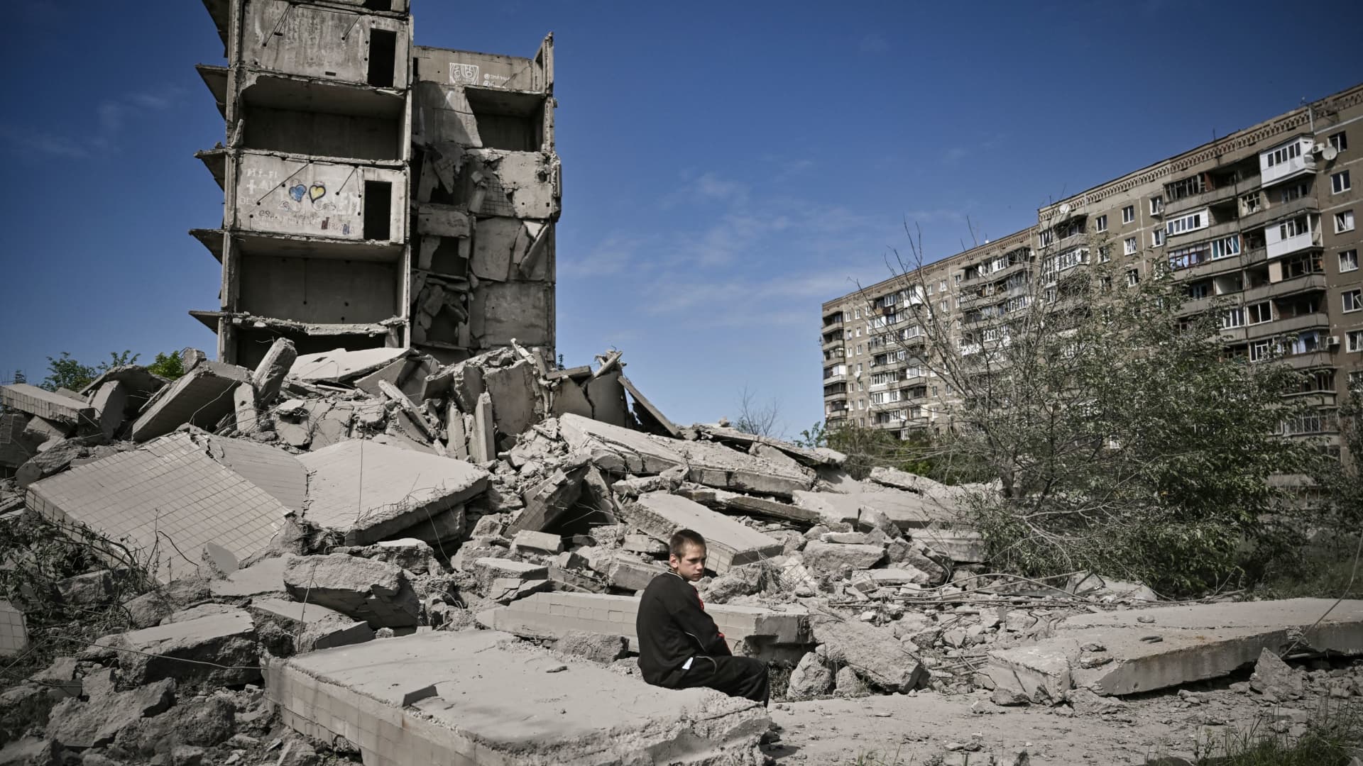 A young boy sits in front of a damaged building after a strike in Donbas, Ukraine, on May 25, 2022. More than 200,000 Ukrainian children have been deported to Russia, President Volodymyr Zelenskyy said in his nightly address.