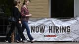 People walk past a "Now Hiring" sign posted outside of a restaurant in Arlington, Virginia on June 3, 2022.