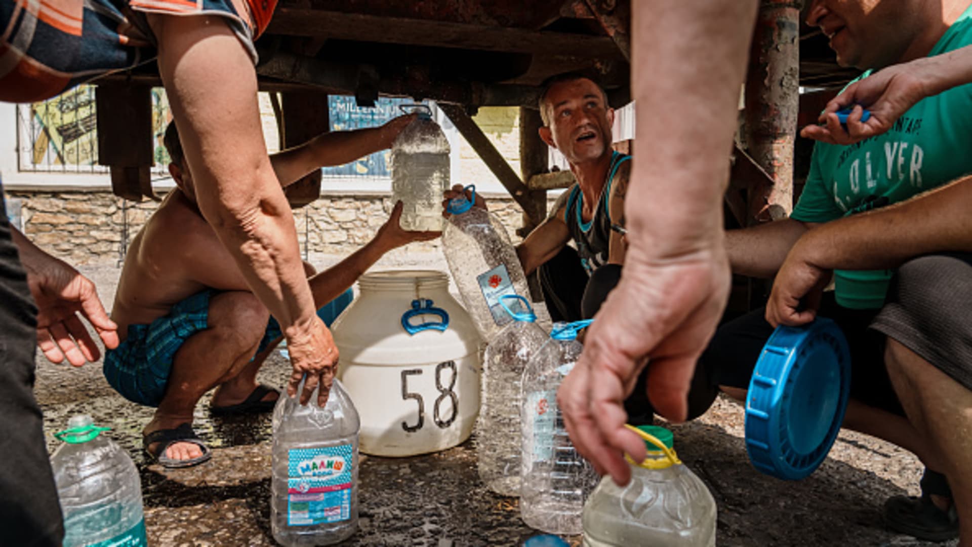 Residents go under the belly of a water truck to collect water as residents have gone without electricity and water for a whole month in Siversk, Ukraine, Sunday, June 5, 2022.