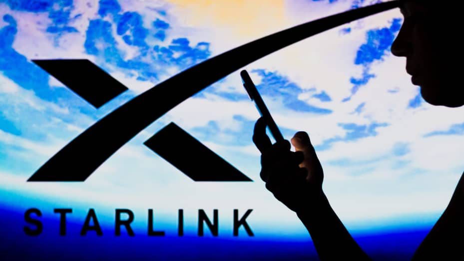 The Starlink logo is seen in the background of a silhouetted woman holding a mobile phone.