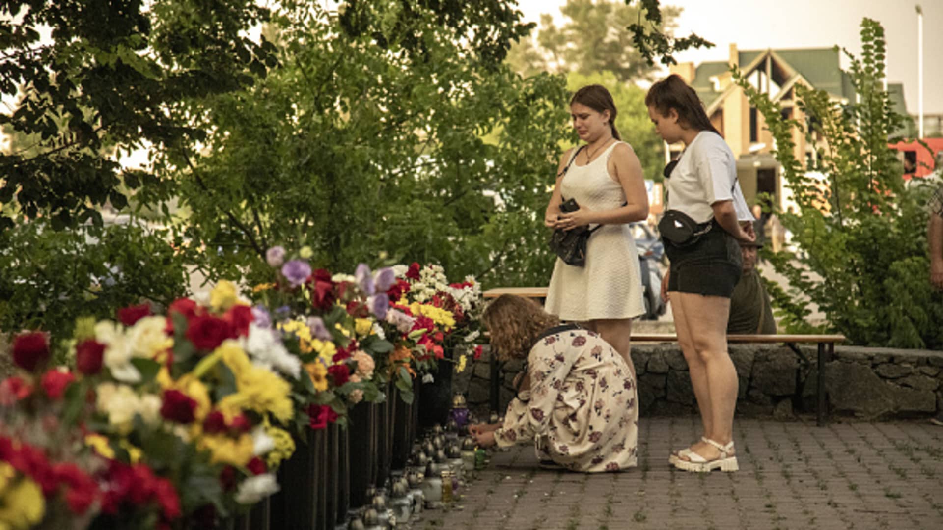 Young women mourn in front of a memorial made of flowers to the civilian victims nearby a shopping mall targeted by a missile strike in Kremenchuk, Ukraine, June 28th, 2022.