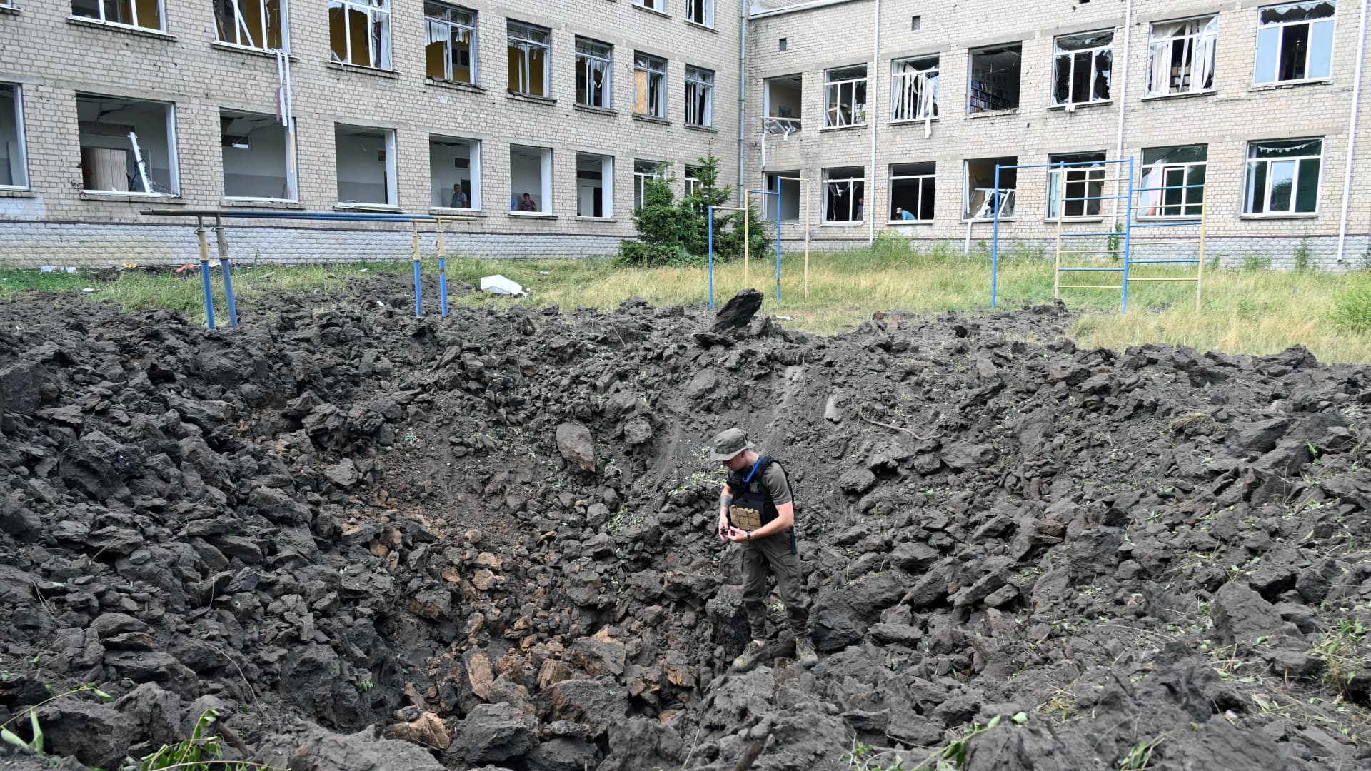 An Ukrainian serviceman examines a crater outside a special comprehensive boarding school for visually impaired children after a strike on its premises, in Kharkiv, on July 7, 2022, amid Russia's military invasion launched on Ukraine.