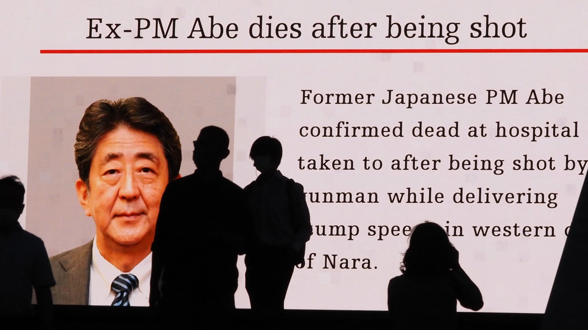 Pedestrians are silhouetted against a large public video screen showing an image of former Japanese prime minister Shinzo Abe in the Akihabara district of Tokyo on July 8, 2022, after he was shot and killed in the city of Nara.