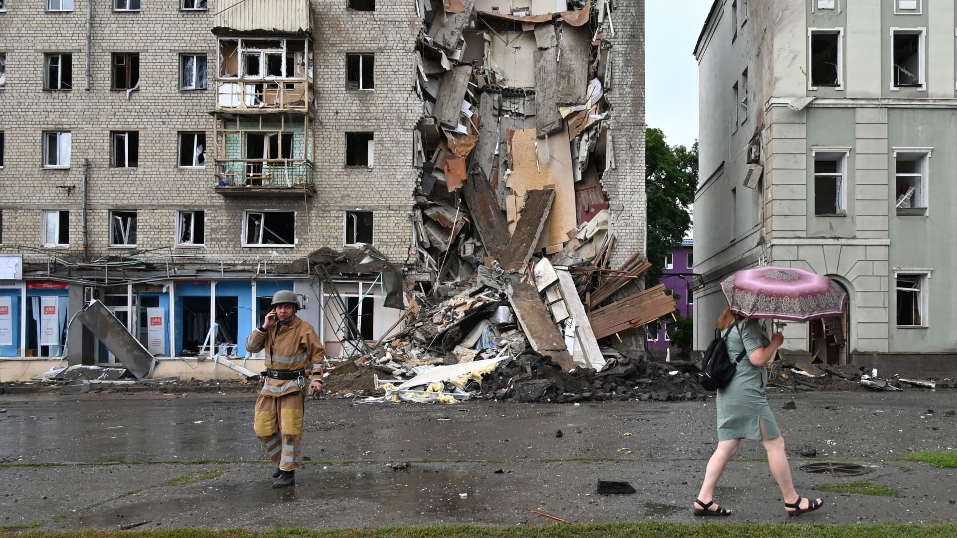 A local resident walks past a Ukrainian rescuer working outside a building partially destroyed after a Russian missile strike in Kharkiv on July 11, 2022, amid Russia's military invasion launched on Ukraine.