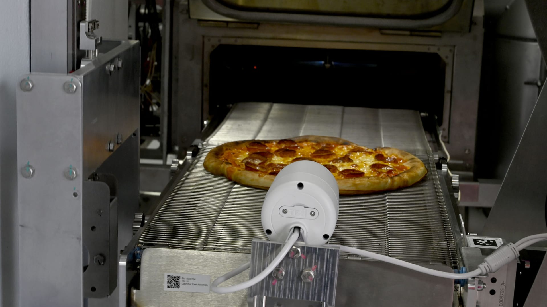 A finished pepperoni pizza exiting a machine made by Stellar Pizza, a robotics-powered mobile pizza restaurant created by a team of former SpaceX engineers