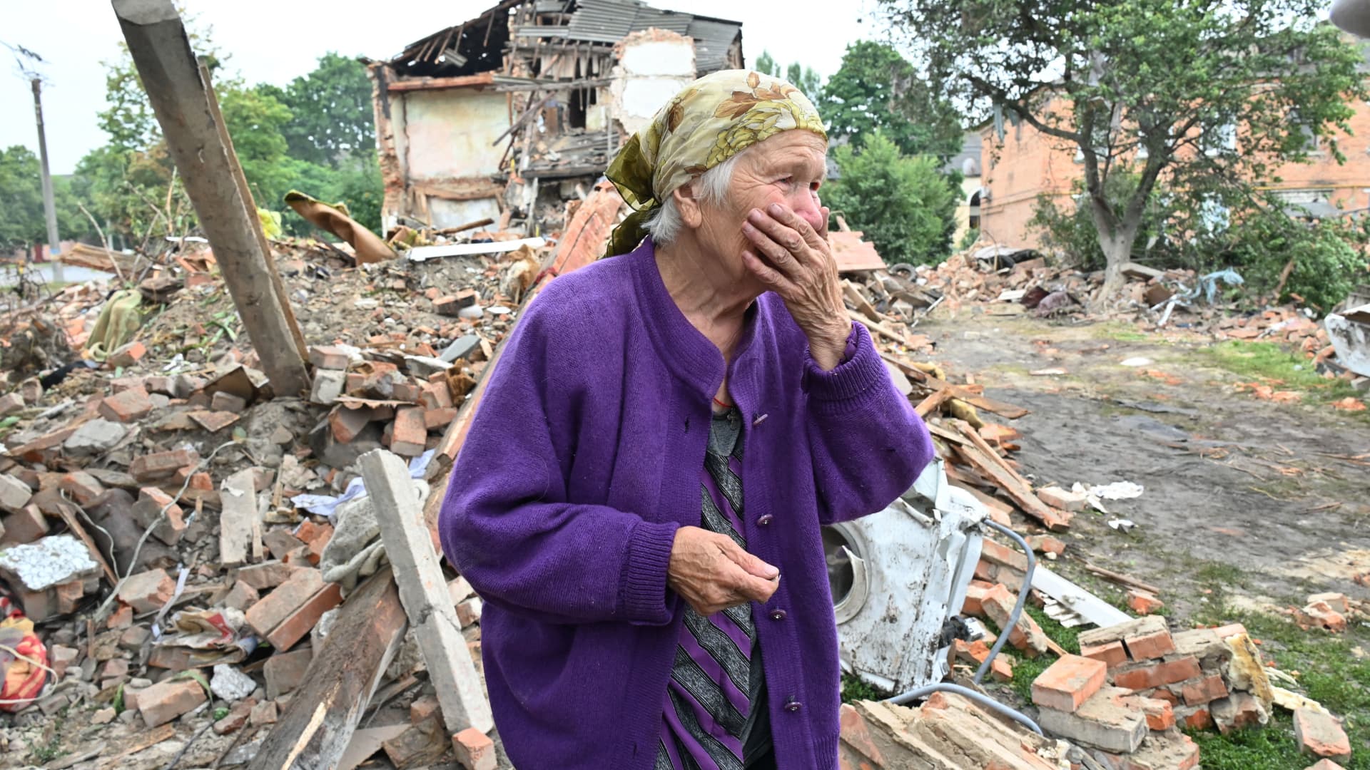 A local resident, Raisa Kuval, 82, reacts next to a damaged building partially destroyed after a shelling in the city of Chuguiv, east of Kharkiv, on July 16, 2022.
