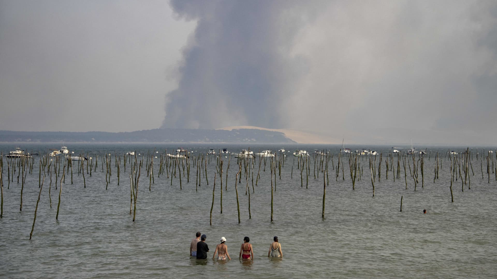 Tourists look at the plume of dark smoke over the Dune of Pilat from Cap Ferret due to a wildfire in a forest near La Teste, southwestern France.
