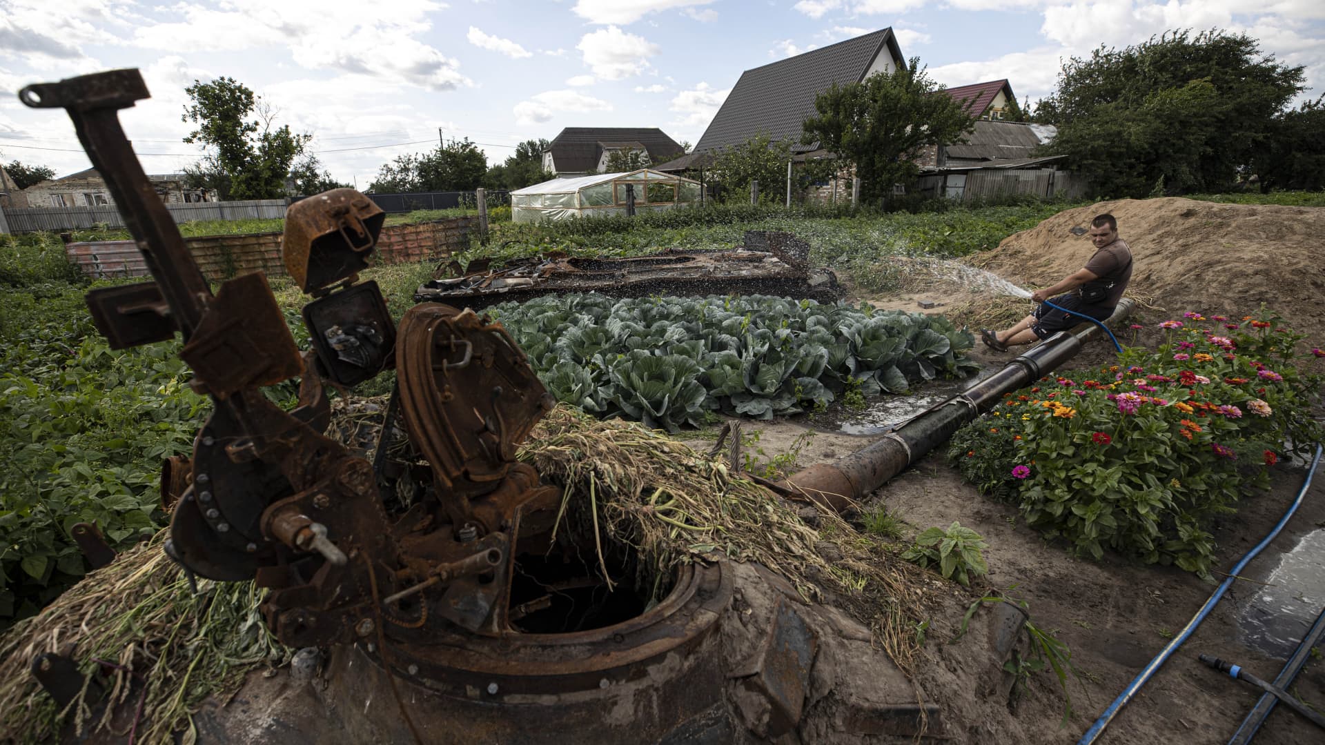 A family grows vegetables in their garden where the wreckage of the tank belonging to the Russian forces is located, in Velyka Dymerka settlement, Kyiv, Ukraine on July 21, 2022. 