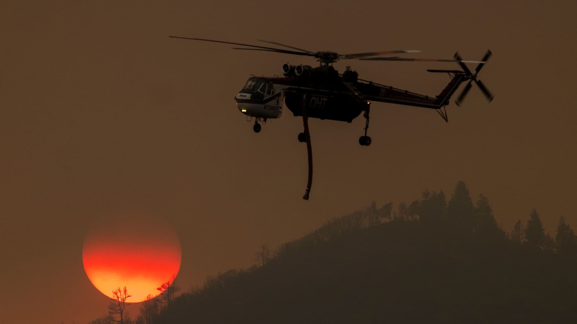A firefighting helicopter passes the setting sun while fighting the Oak Fire near Mariposa, California, on July 24, 2022.