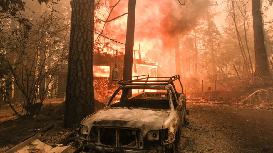 A structure burns behind a charred vehicle on Jerseydale road during the Oak Fire in Mariposa County, California, US, on Saturday, July 23, 2022.