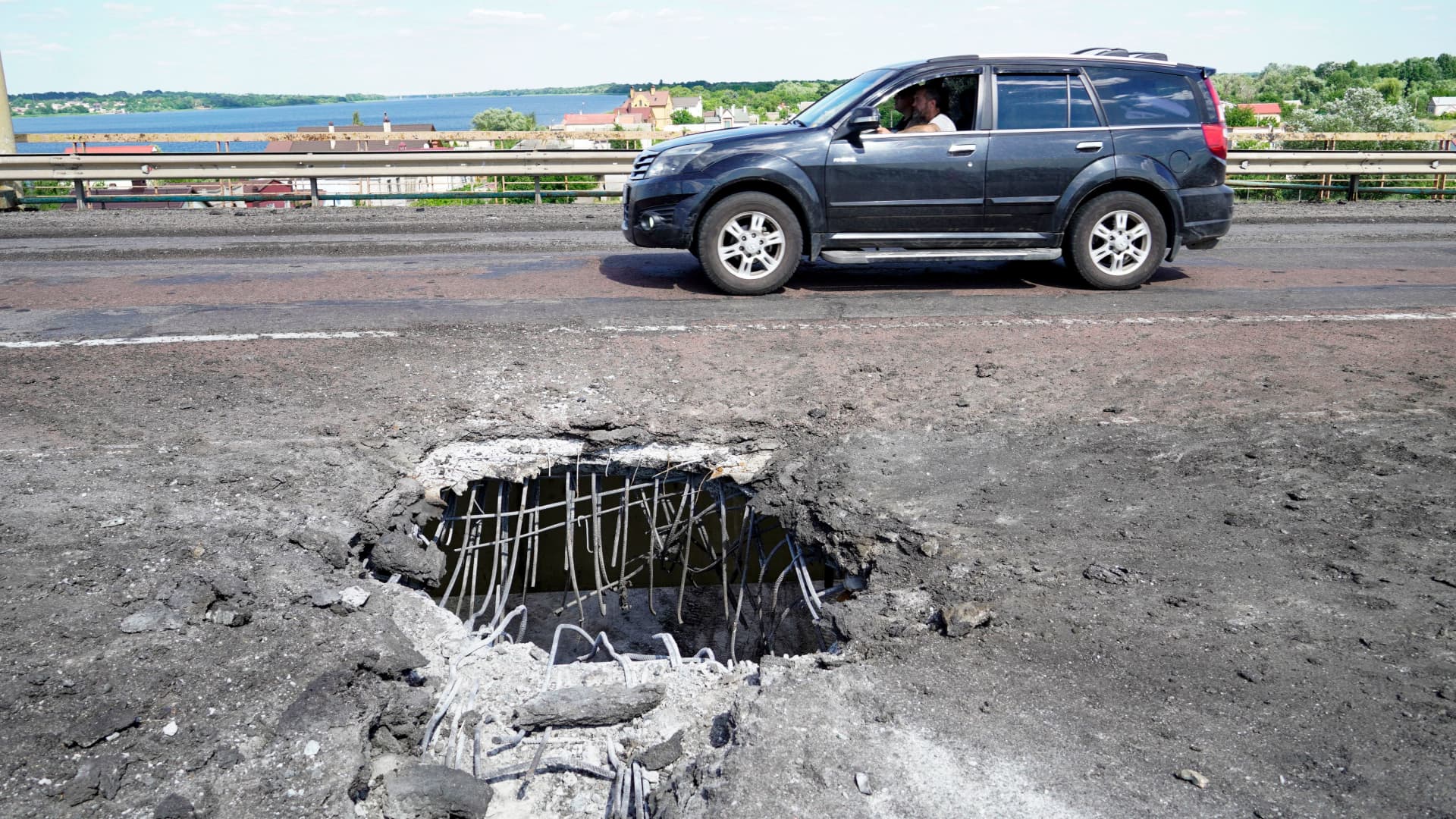 A picture taken on July 21, 2022 shows a car moving past a crater on Kherson's Antonovsky bridge across the Dnipro river caused by a Ukrainian rocket strike, amid the ongoing Russian military action in Ukraine.