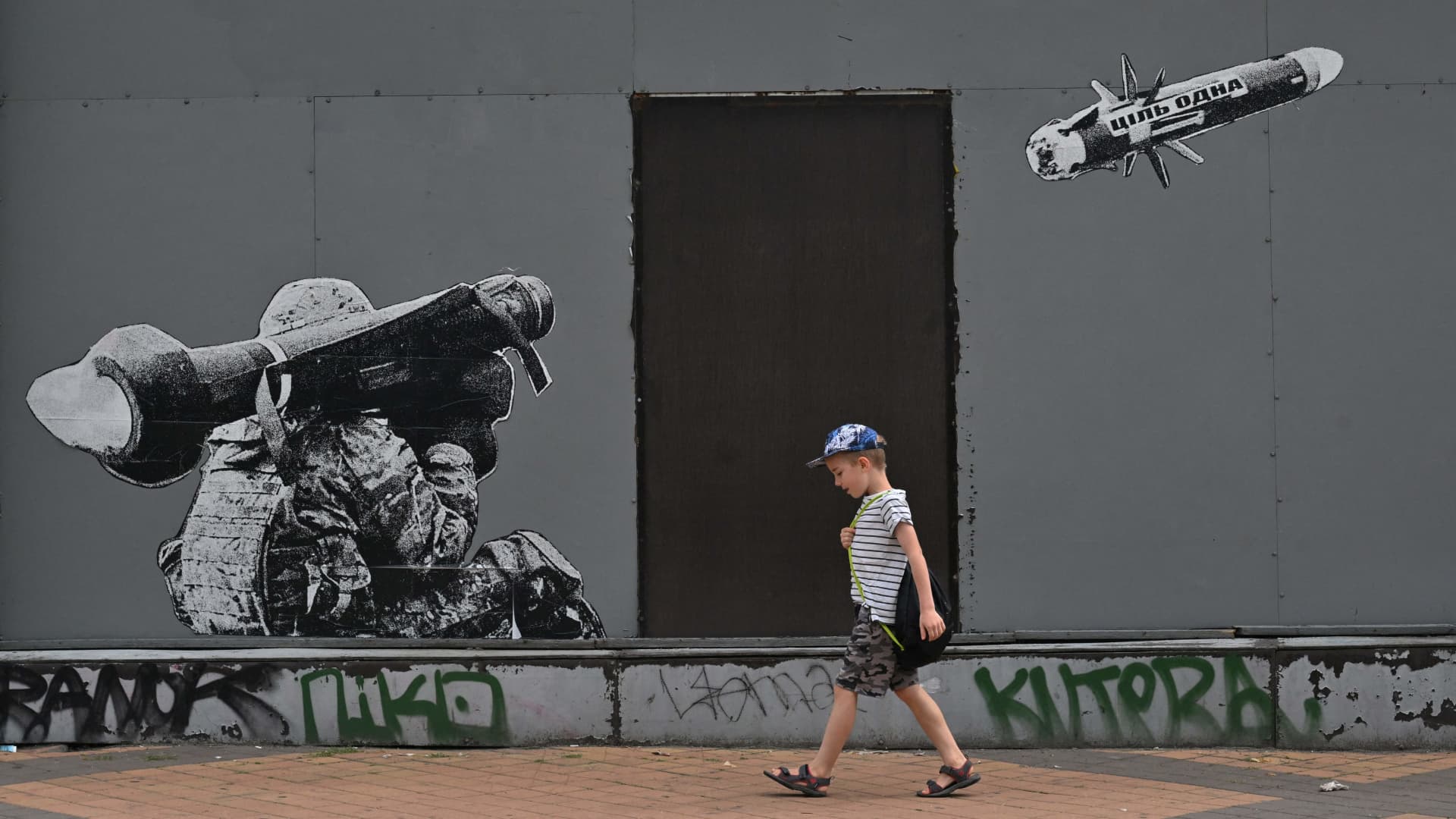 A boy walks past a graffiti on a wall depicting a Ukrainian serviceman making a shot with a US-made Javelin portable anti-tank missile system, in Kyiv, on July 29, 2022.