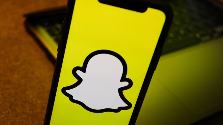 Snapchat logo displayed on a phone screen is seen with a laptop in the background in this illustration photo taken in Krakow, Poland on August 10, 2022.