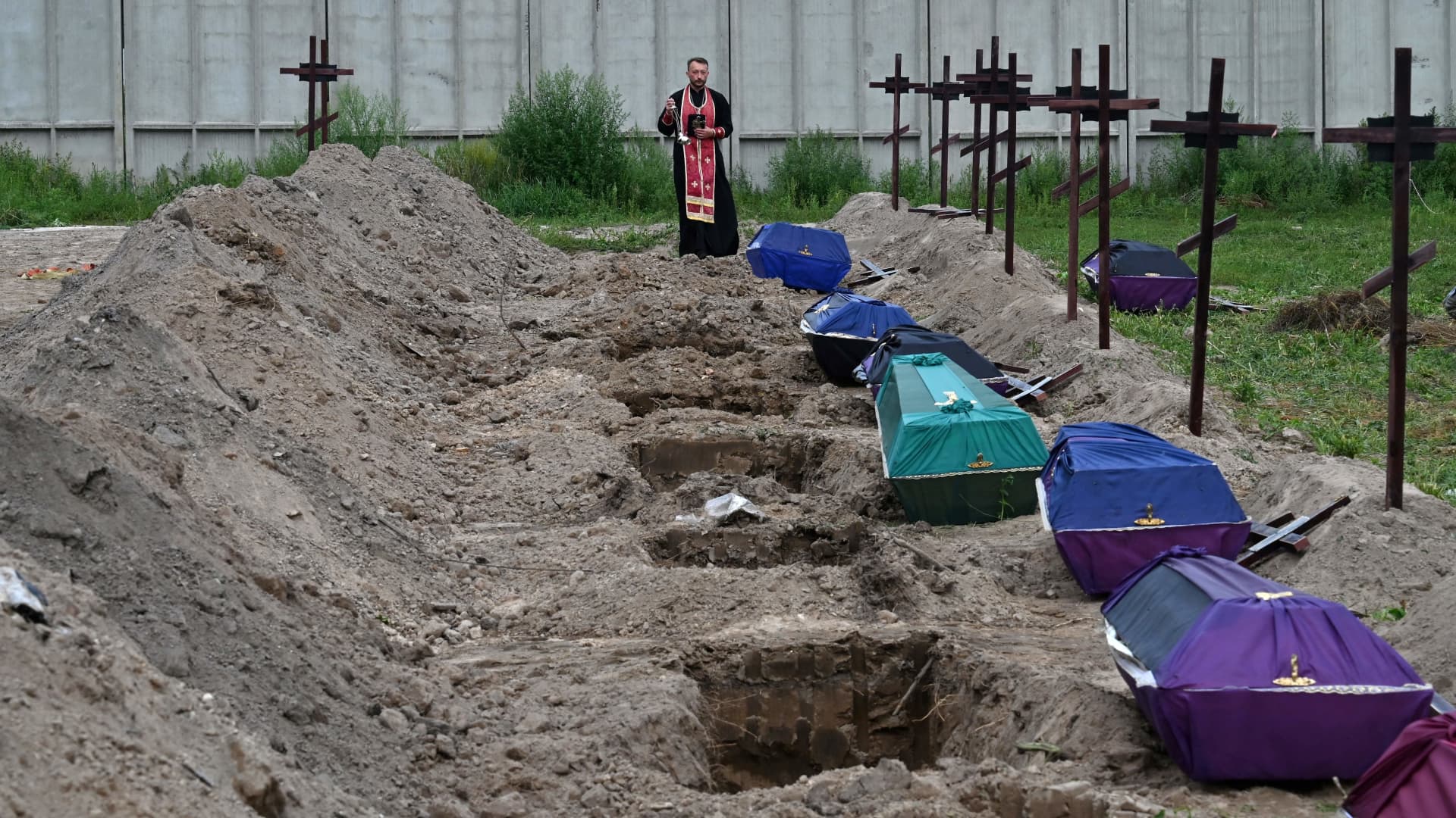 An Orthodox priest serves at the graves of unidentified civilians during their funeral at a local cemetary in the city of Bucha, Kyiv region, on August 11, 2022. 