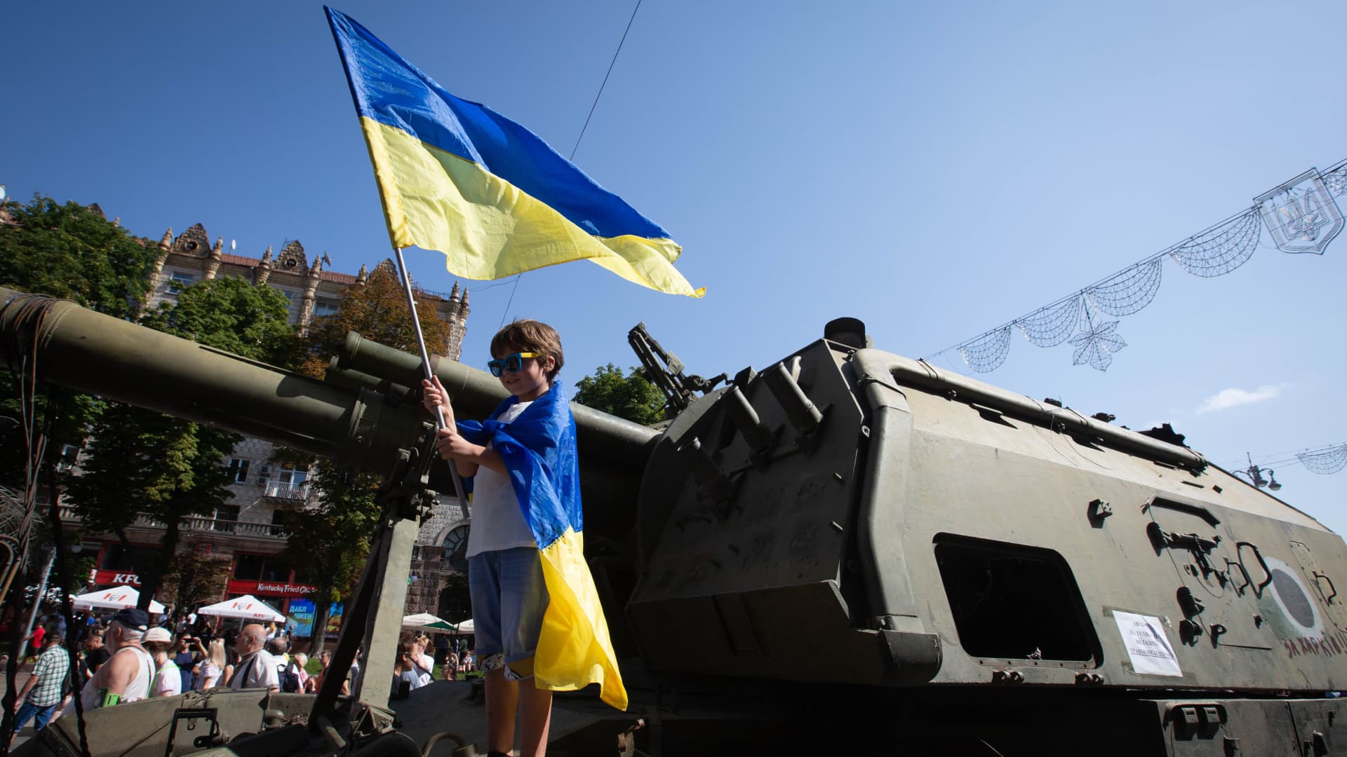A boy with Ukrainian national flags poses for a photo while standing on a destroyed Russian military vehicle displayed on the main street Khreshchatyk as part of the upcoming celebration of the Independence Day of Ukraine amid Russia's invasion of Ukraine in central Kyiv. 