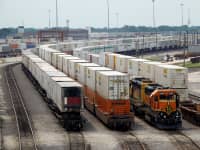 Shipping containers sit at a railway facility waiting to be transferred.
