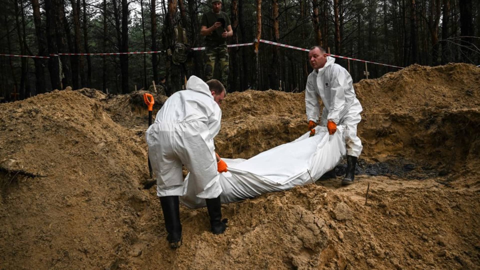 EDITORS NOTE: Graphic content / TOPSHOT - Two forensic technicians carry a body bag in a forest on the outskirts of Izyum, eastern Ukraine on September 16, 2022.