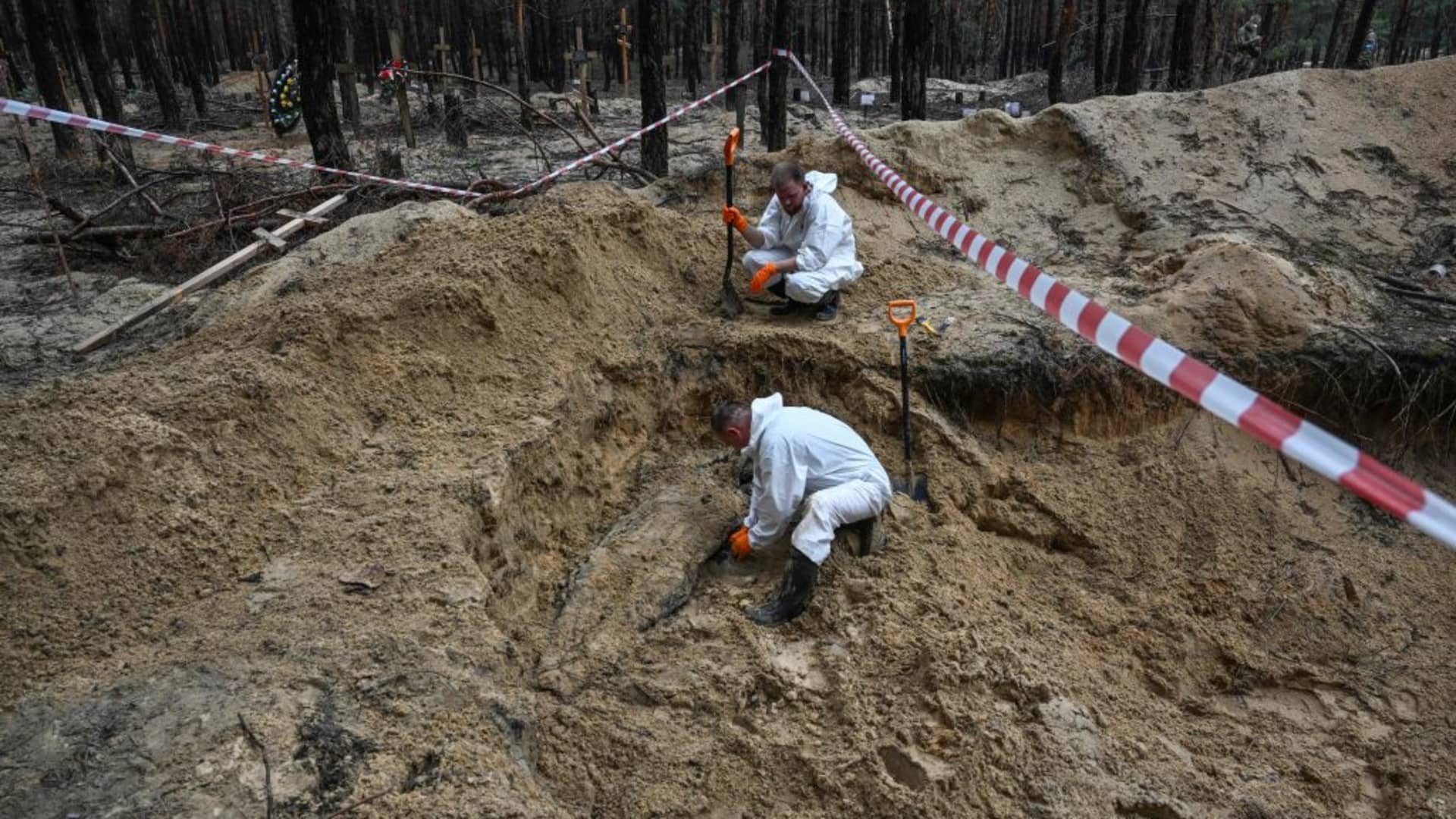Two forensic technicians uncover a body in a forest on the outskirts of Izyum, eastern Ukraine on September 16, 2022.