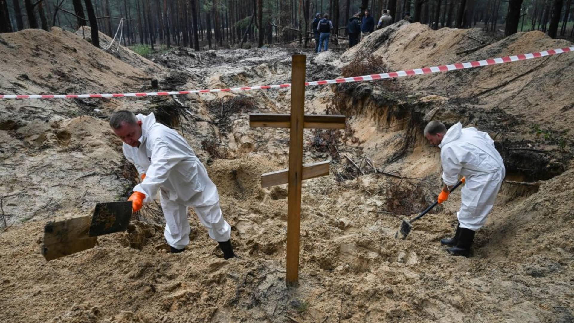 Two forensic technicians dig near a cross in a forest on the outskirts of Izyum, eastern Ukraine on September 16, 2022.