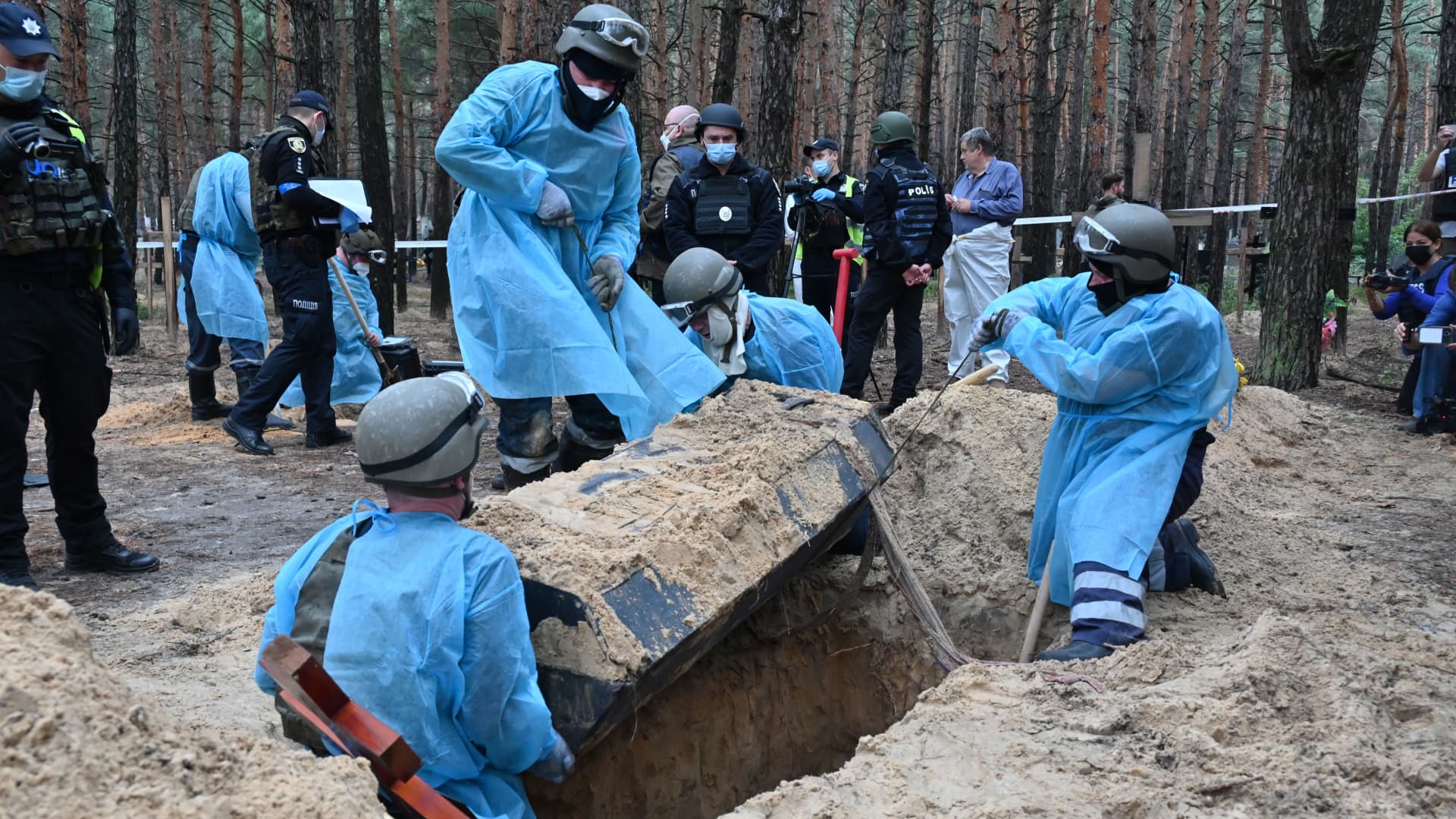 Forensic technicians uncover a coffin in a forest on the outskirts of Izyum, eastern Ukraine on September 16, 2022. - Ukraine said on September 16, 2022 it had counted 450 graves at just one burial site near Izyum after recapturing the eastern city from the Russians.