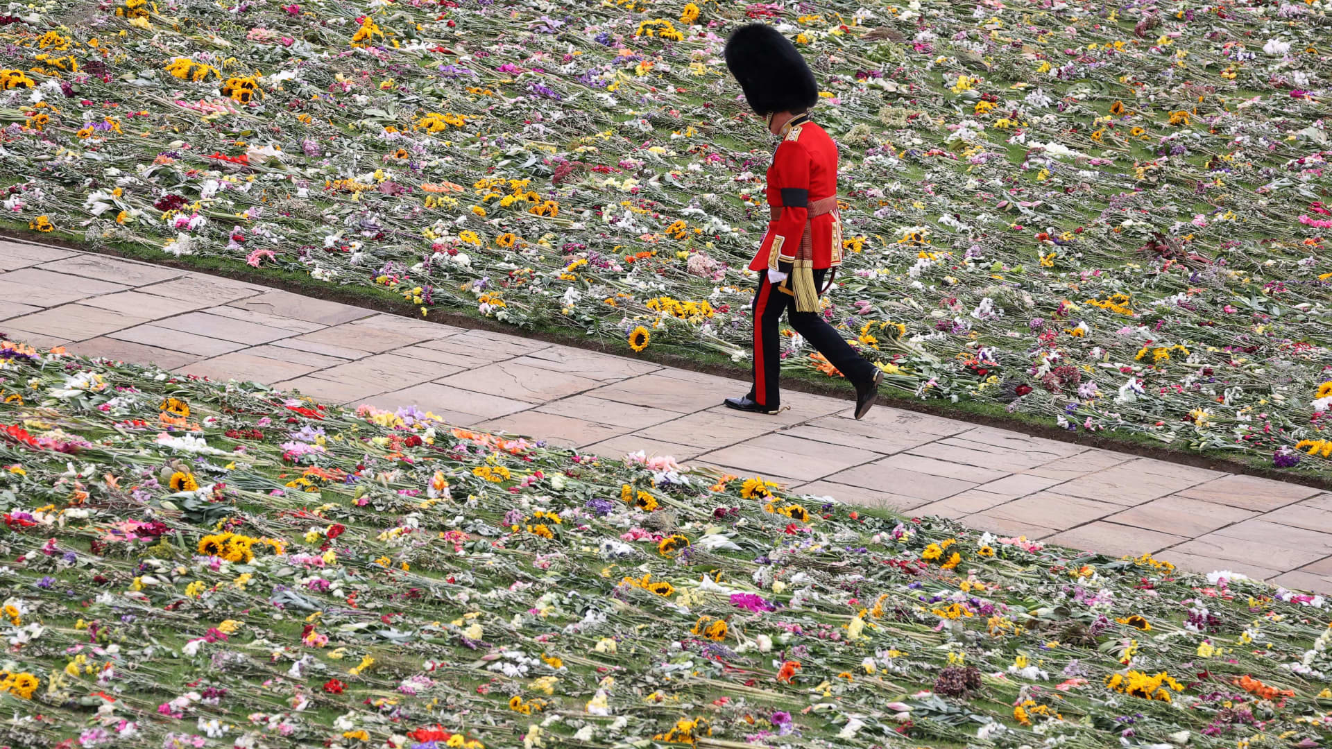 A King's Guard soldier walks along the lawn covered with flowers at the Windsor Castle on September 19, 2022 in Windsor, England on the day of the state funeral for Queen Elizabeth II.