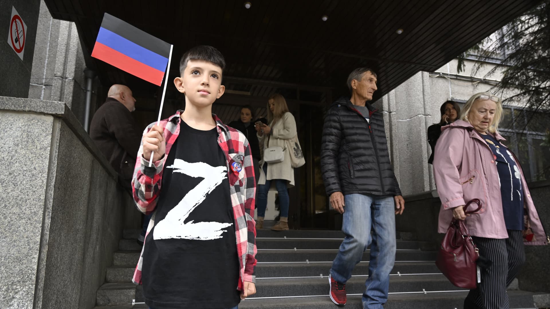 A boy wearing a T-shirt with the letter 'Z', the tactical insignia of Russian troops in Ukraine, and holding a flag of the self-proclaimed Donetsk People's Republic (DNR) - the eastern Ukrainian breakaway region - stands at the entrance to the DNR embassy in Moscow on September 23, 2022, as Moscow-held regions of Ukraine vote in annexation referendums that Kyiv and its allies say are illegal and illegitimate.
