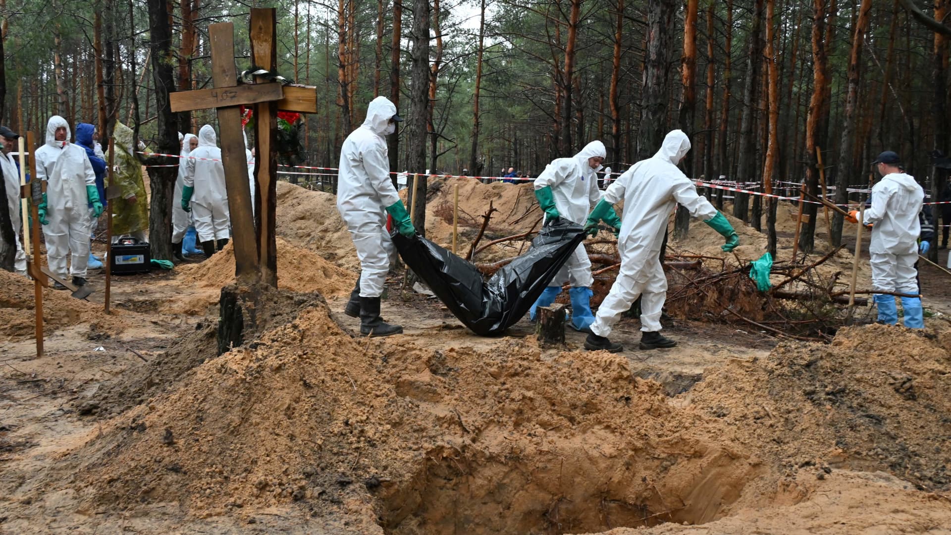 Investigators carry away a body bag in a forest near Izyum, eastern Ukraine, on September 23, 2022, where Ukrainian investigators have uncovered more than 440 graves after the city was recaptured from Russian forces, bringing fresh claims of war atrocities.