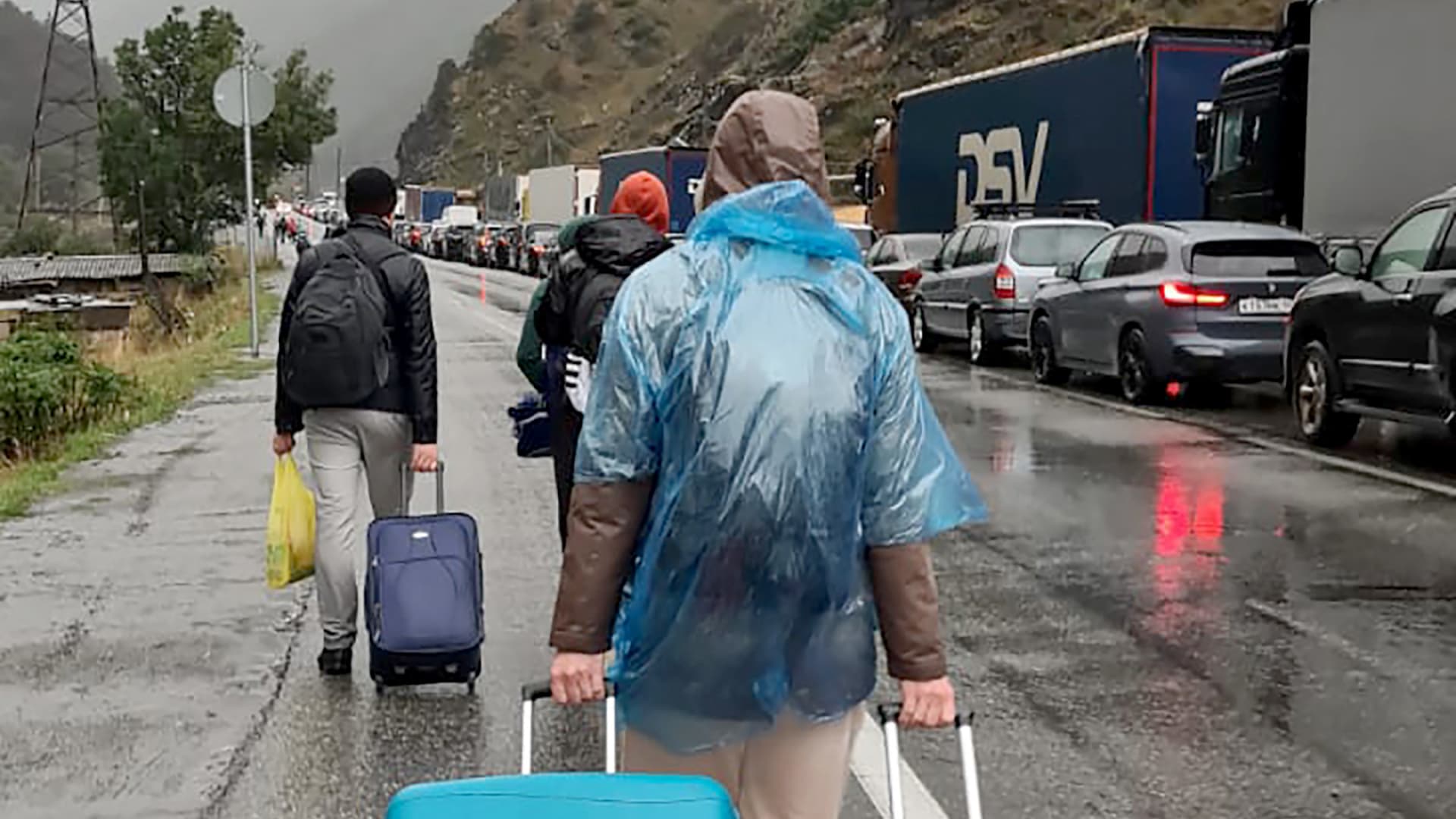 People carrying luggage walk past vehicles with Russian license plates on the Russian side of the border towards the Nizhniy Lars customs checkpoint between Georgia and Russia some 25 km outside the town of Vladikavkaz, on September 25, 2022.