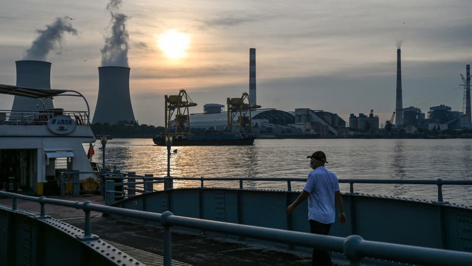 A man walks towards a ferry as the Wujing coal-electricity power station is seen across the Huangpu River in the Minhang district of Shanghai on August 22, 2022. (Photo by Hector RETAMAL / AFP) (Photo by HECTOR RETAMAL/AFP via Getty Images)