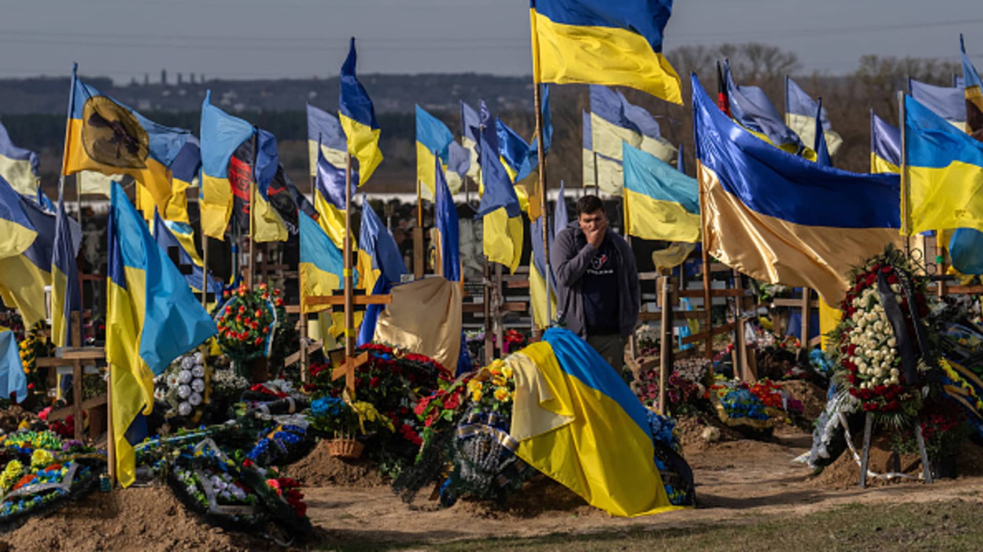 A man pauses by a grave as Ukrainian flags fly in a cemetery for soldiers killed in action following the Russian invasion earlier this year, on October 19, 2022 in Kharkiv, Ukraine. Russia's president Vladimir