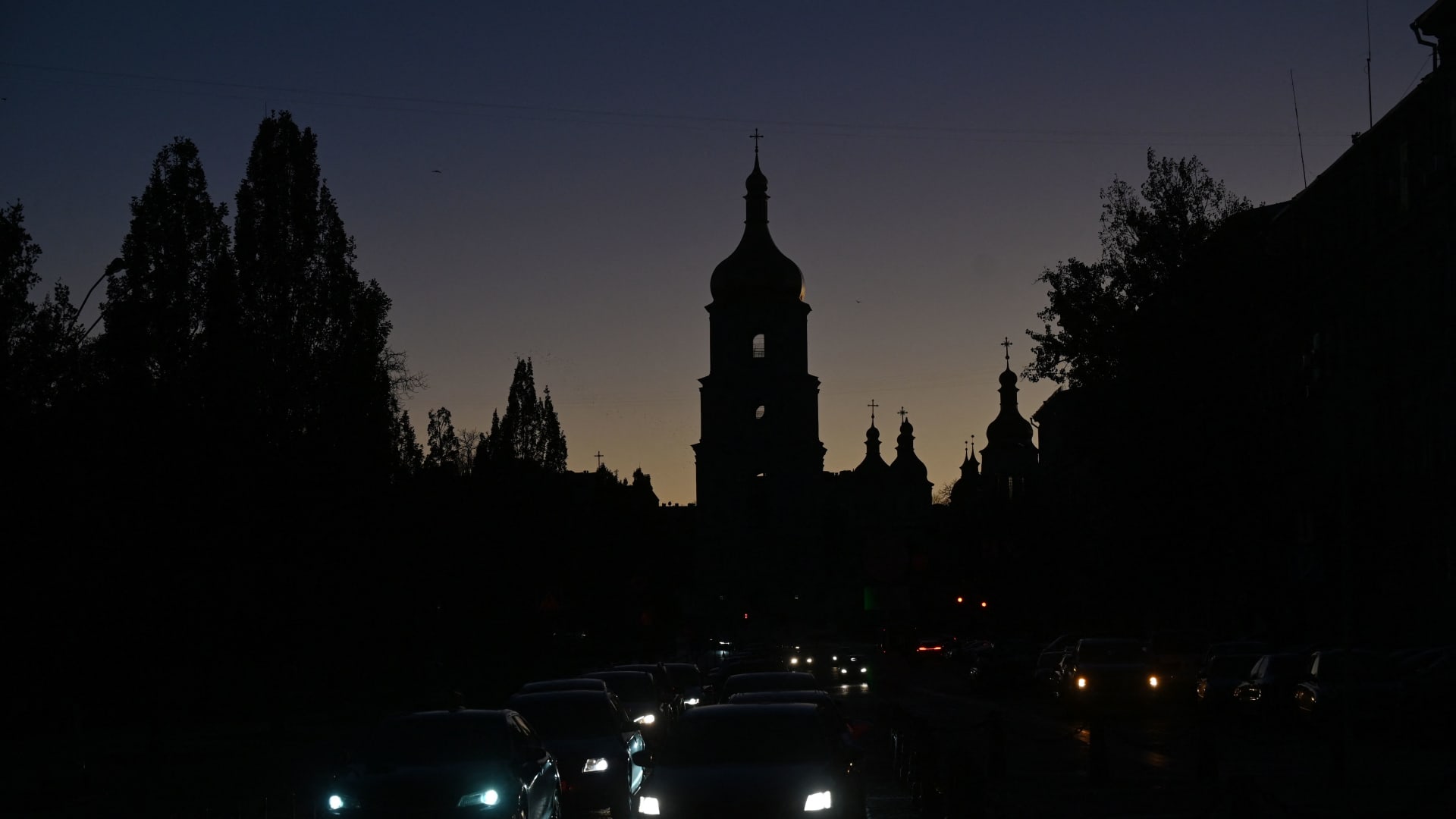 Vehicles drive along a street with St. Sophia Cathedral in the background, as the city is plunged into near darkness following a military strike that partially brought down the power infrastructure, in Kyiv on Oct. 31, 2022.