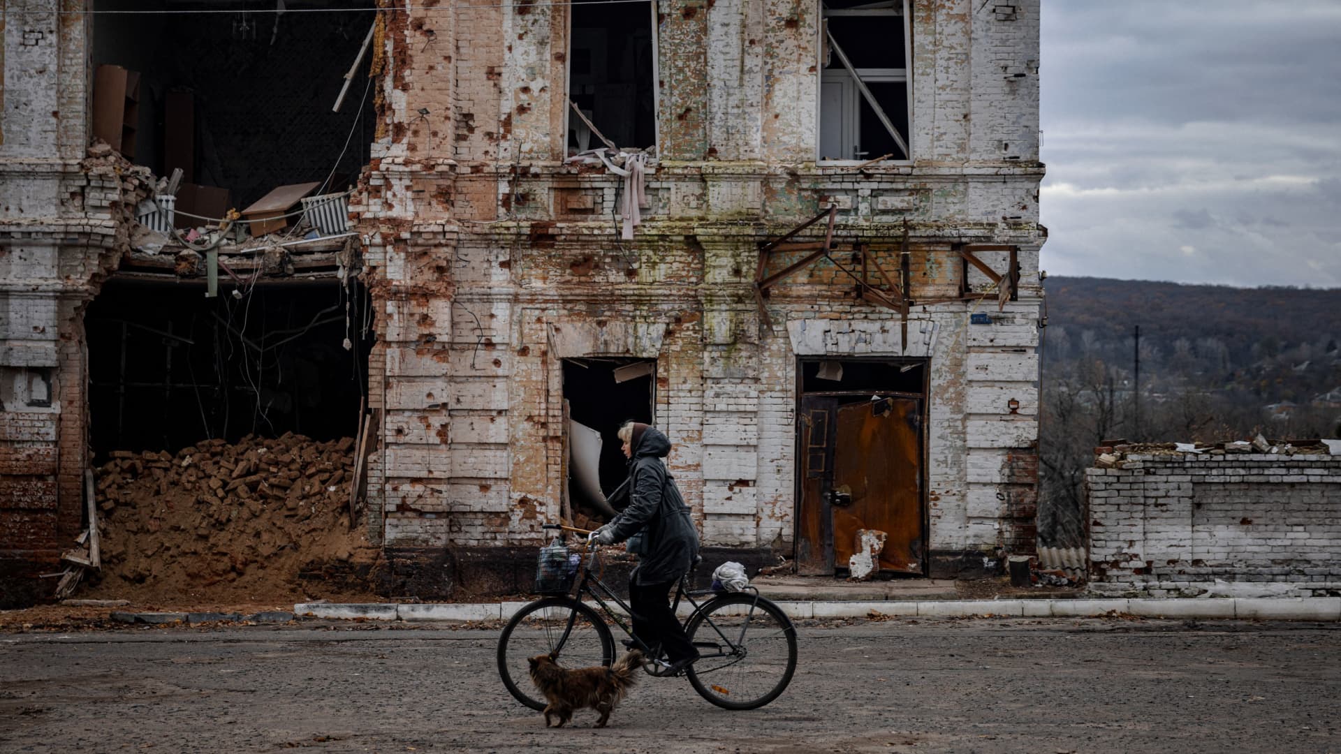 A woman rides a bicycle past a damaged building in the town of Kupiansk on Nov. 3, 2022, Kharkiv region, amid the Russian invasion of Ukraine.