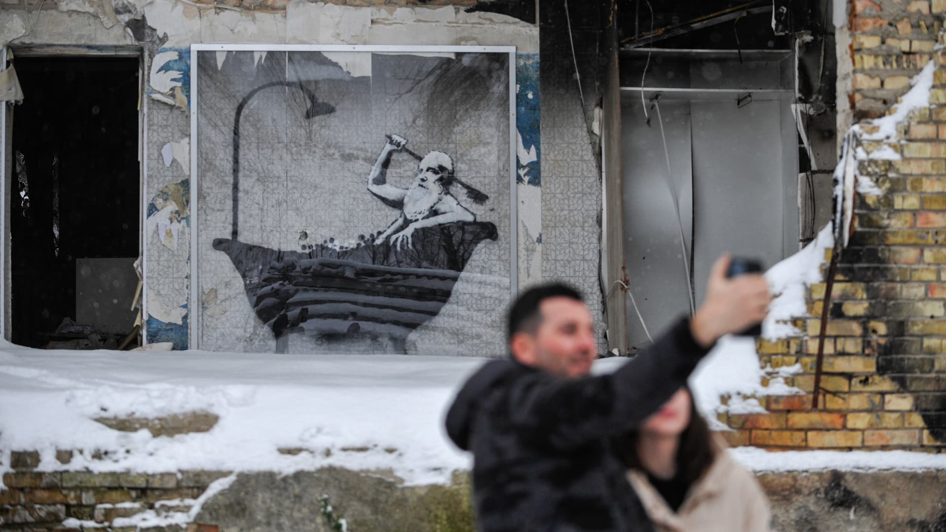 People take pictures in the background of graffiti by the famous anonymous street artist Banksy which is shown on one of the apartment buildings destroyed by the Russian army in Gorenka.