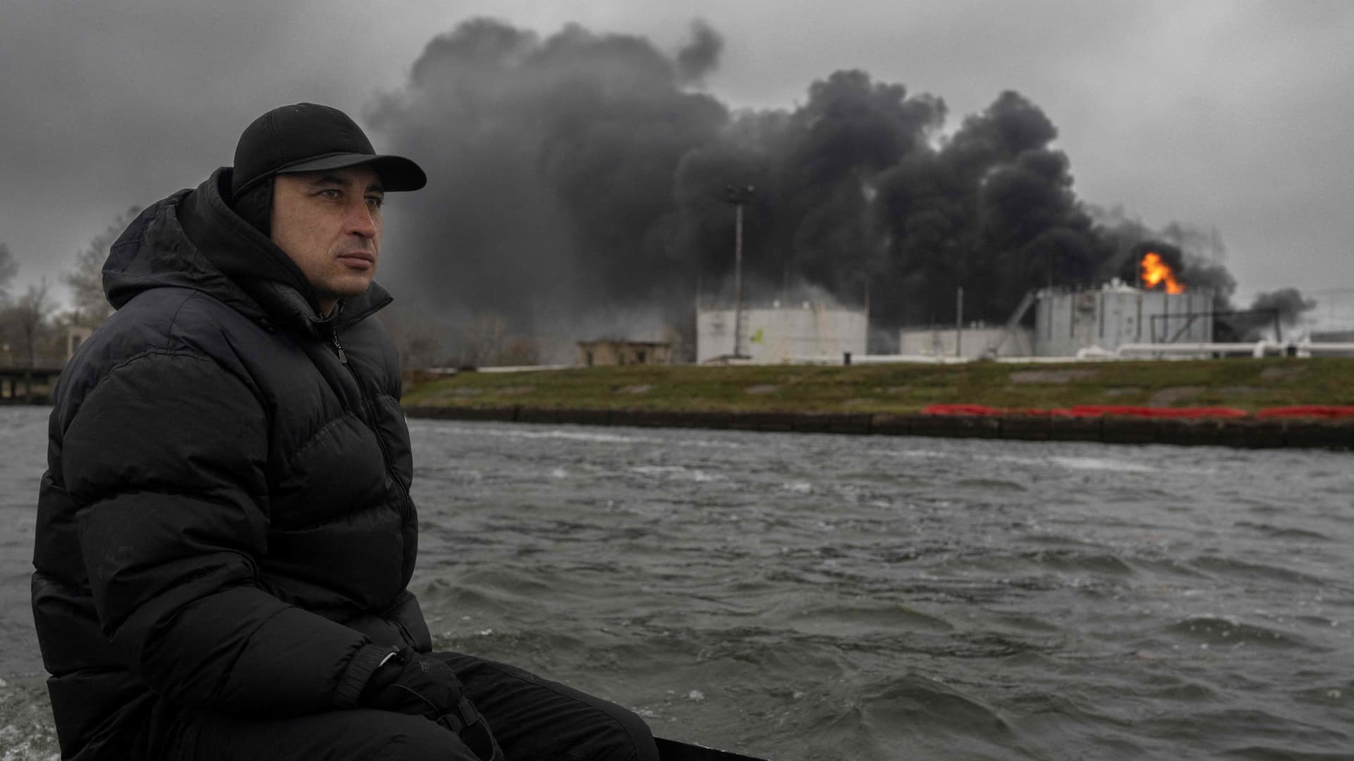 A fisherman sails his boat on the Dnipro River as black smoke rises after an attack on an oil reserve in Kherson, on November 20, 2022, amid the Russian invasion of Ukraine.