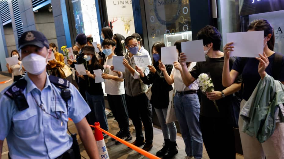 People hold white sheets of paper and flowers in a row as police check their IDs during a protest over coronavirus disease (COVID-19) restrictions in mainland China, during a commemoration of the victims of a fire in Urumqi, in Hong Kong, China November 28, 2022. REUTERS/Tyrone Siu