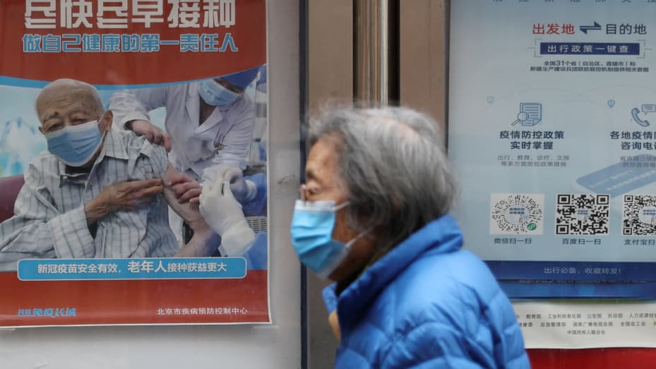 A person walks past a poster encouraging elderly people to get vaccinated against the coronavirus disease (COVID-19), near a residential compound in Beijing, China March 30, 2022. Picture taken March 30, 2022. REUTERS/Tingshu Wang