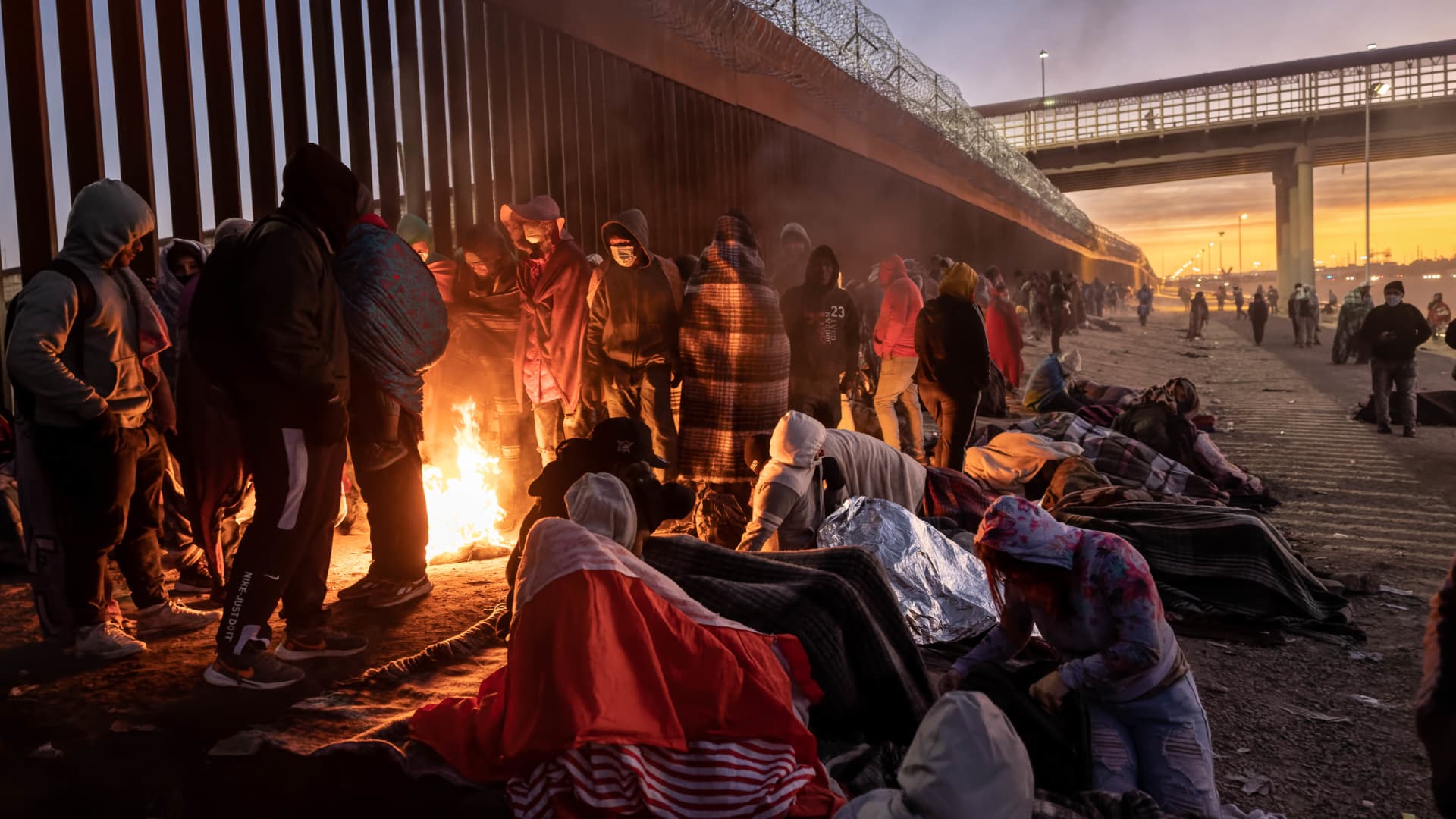 Immigrants keep warm by a fire at dawn after spending the night outside next to the U.S.-Mexico border fence on December 22, 2022 in El Paso, Texas.
