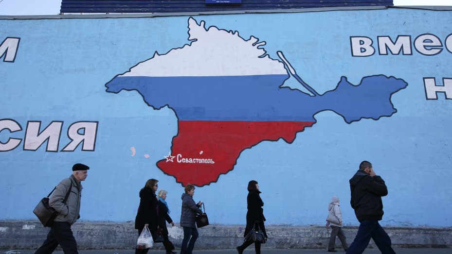 Pedestrians pass a giant wall mural showing a map of the Crimean peninsula filled with the flag of the Russian Federation, in support of the Russian annexation, in Moscow, Russia, on Friday, March 28, 2014. Foreign companies face the prospect of untangling from a country that's become a key trading partner with close financial ties to the West, as U.S. President Barack Obama and German Chancellor Angela Merkel threaten economic retaliation for Russia's moves to annex the Crimean peninsula. Photographer: And