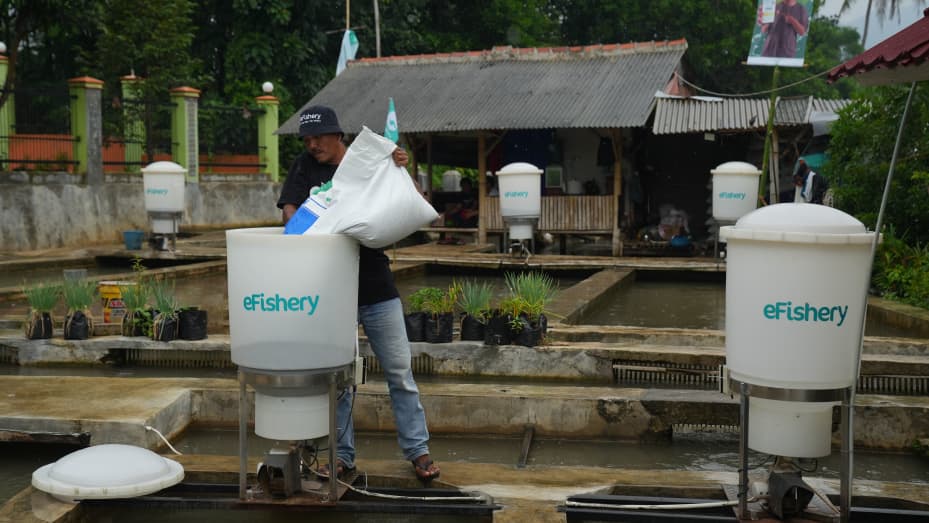 A worker refills a robotic dispenser by eFishery, an agritech startup, at a fish farm in Subang Regency in West Java, Indonesia, in June 2022. The startup helps farmers optimize their processes through automatic feeders and mobile apps.