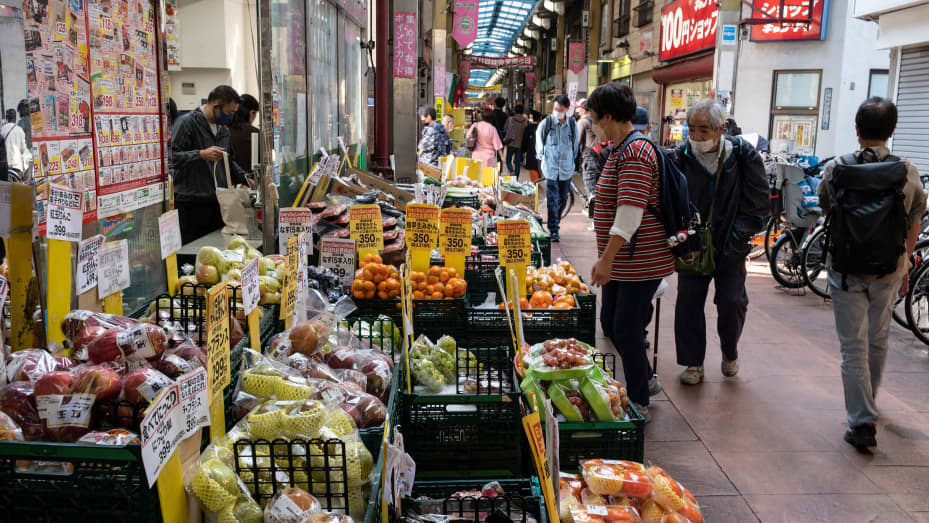 Esta foto tomada el 23 de octubre de 2022 muestra a personas mirando frutas y verduras afuera de un supermercado a lo largo de una calle comercial cubierta en Tokio.