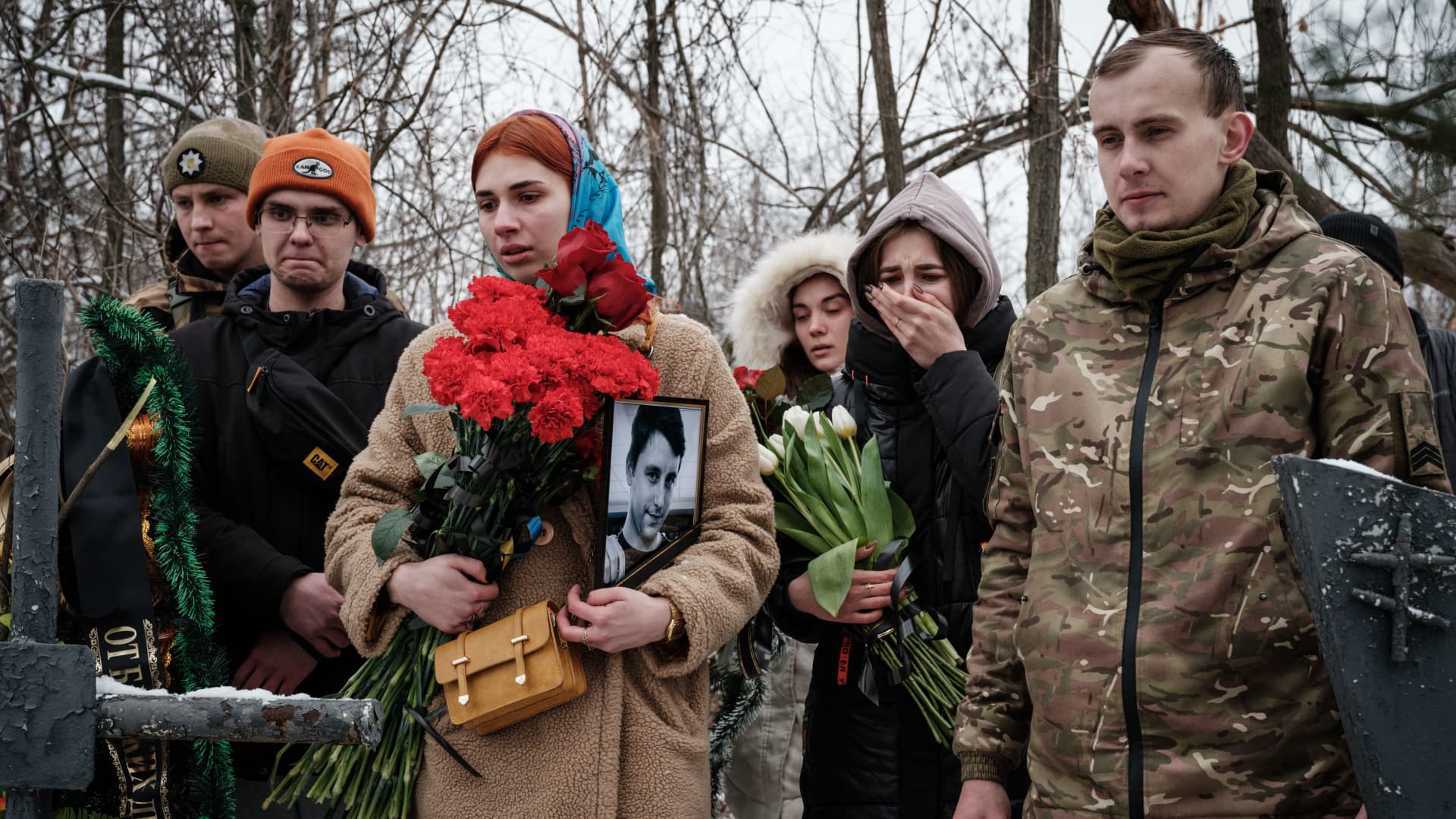 Kateryna Avdeyeva (C), holds a portrait of her late friend, Ukrainian serviceman of the Azov battalion killed in action in Bakhmut, 28-year-old orphan Oleksandr Korovniy, as she attends his funeral ceremony at a cemetery in Sloviansk on January 30, 2023, amid the Russian invasion of Ukraine. 
