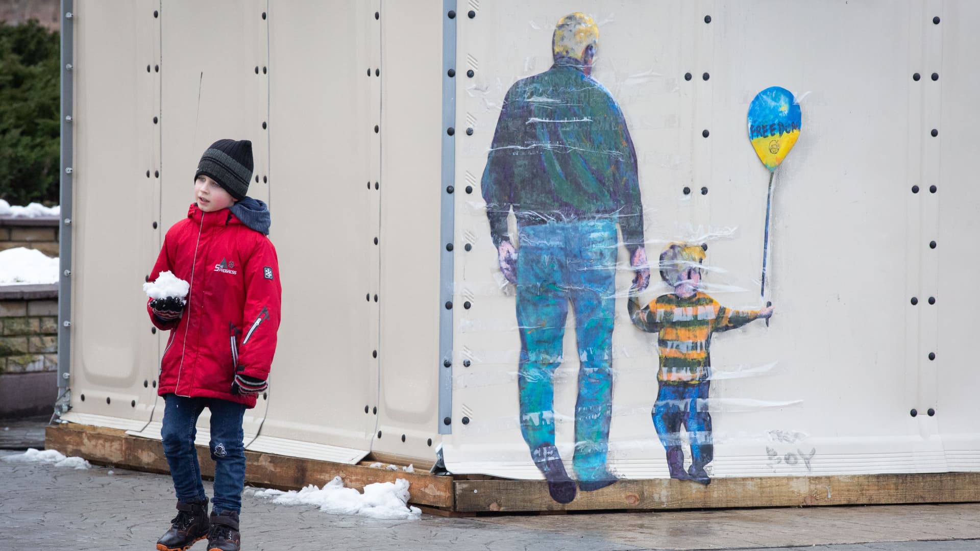 A boy stands next to an art work by famous Italian street artist Tvboy in the center of the town of Bucha, near Kyiv, Ukraine, on February 2, 2023. 