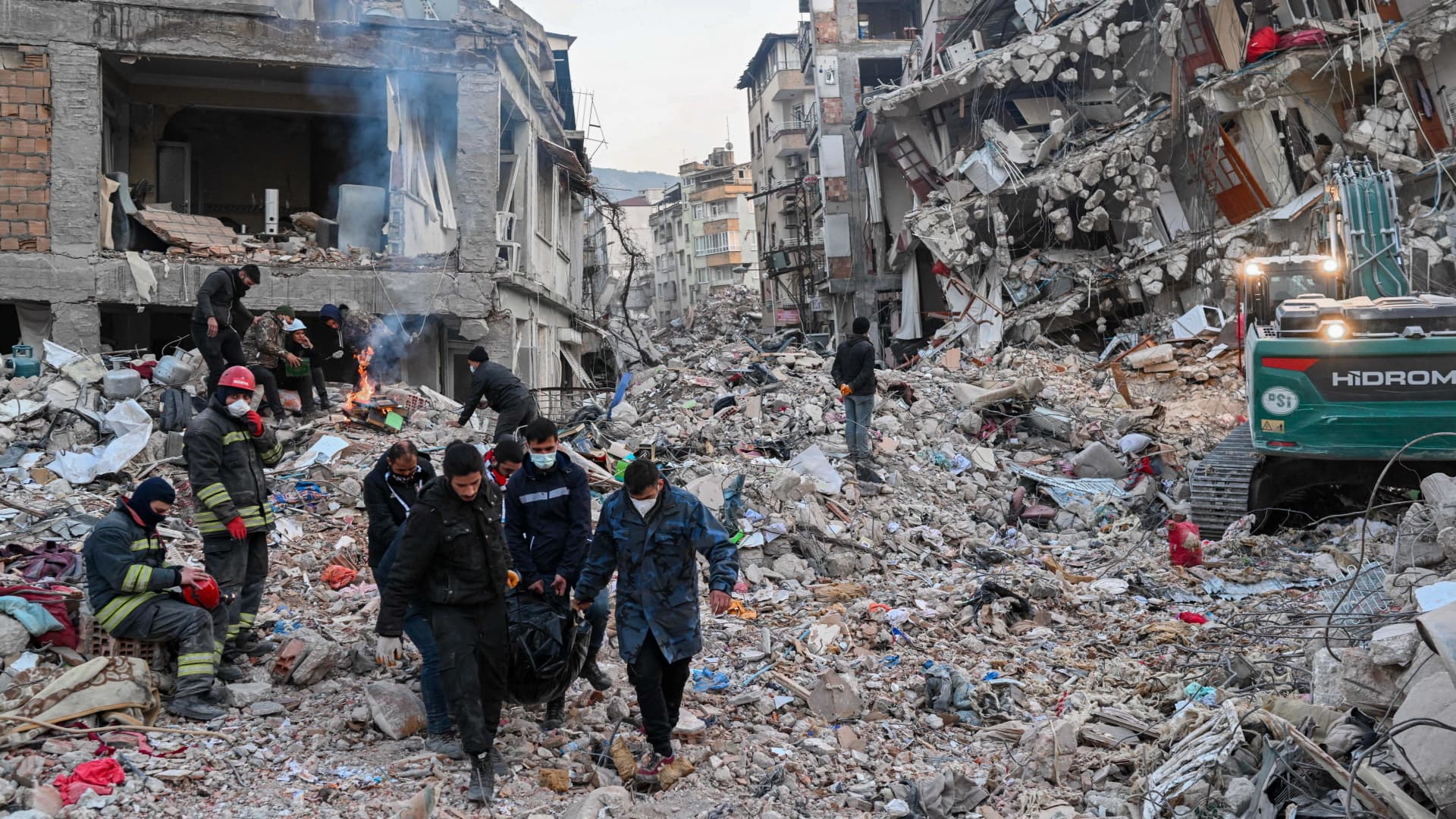 People carry a bodybag as local residents wait for their relatives to be pulled out from the rubble of collapsed buildings in Hatay, on February 14, 2023, after a 7.8-magnitude earthquake struck the country's south-east.